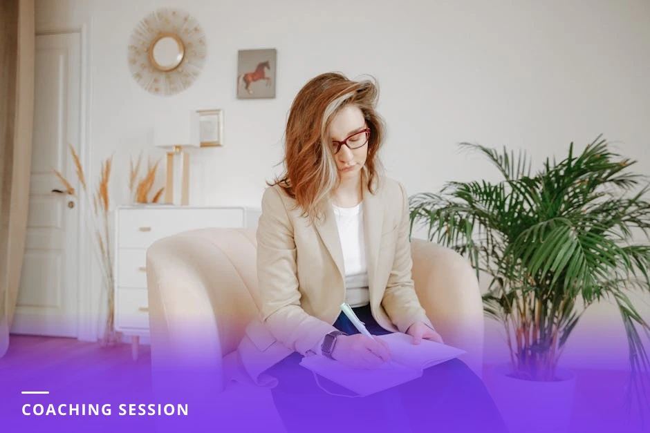 Coach in a bright Scandinavian office listens attentively and takes notes on a notepad while a client speaks across a small table, natural light through large windows.