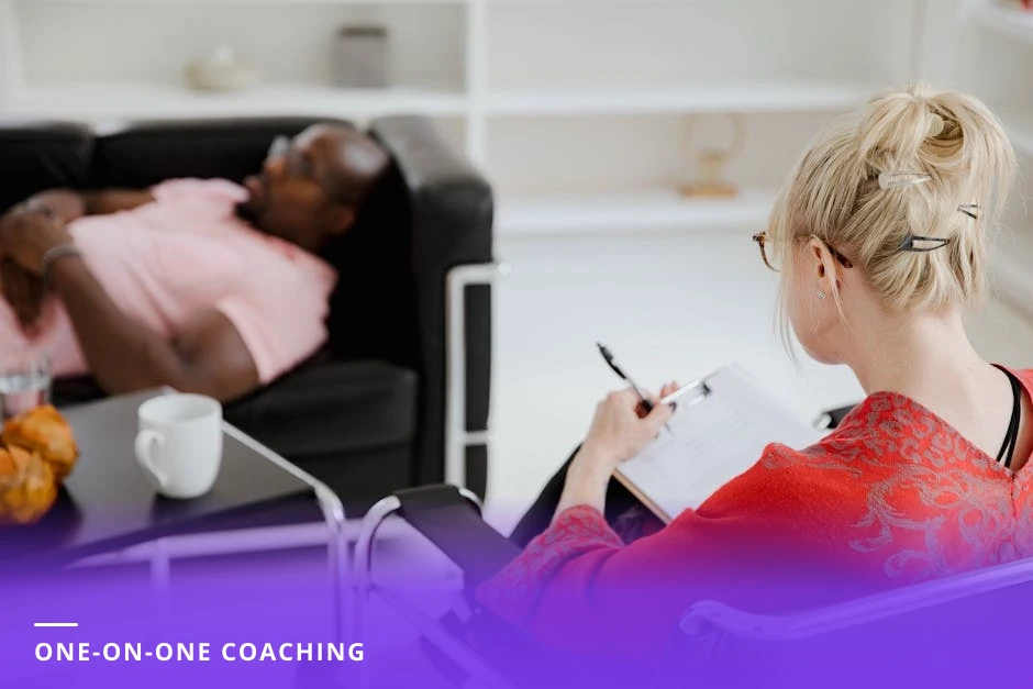 Two professionals in a European office leaning over a laptop and printed notes as the coach points to a list, candid one-on-one discussion in natural light