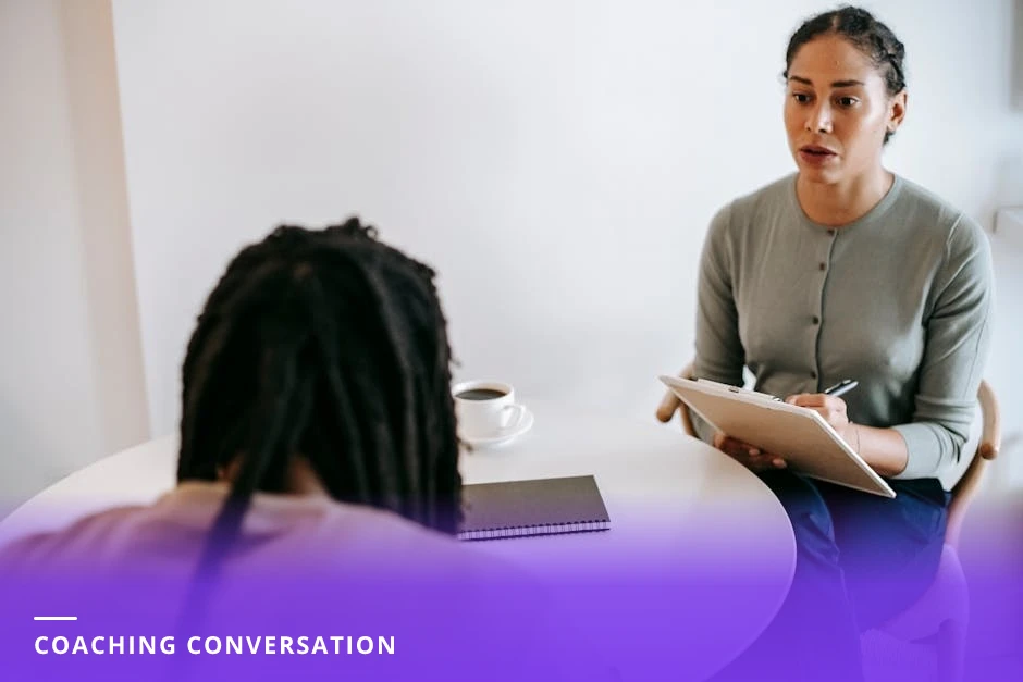 Coach and client at a sunlit cafe table, coach listening attentively and jotting notes in a notebook while client gestures, coffee cups on the table
