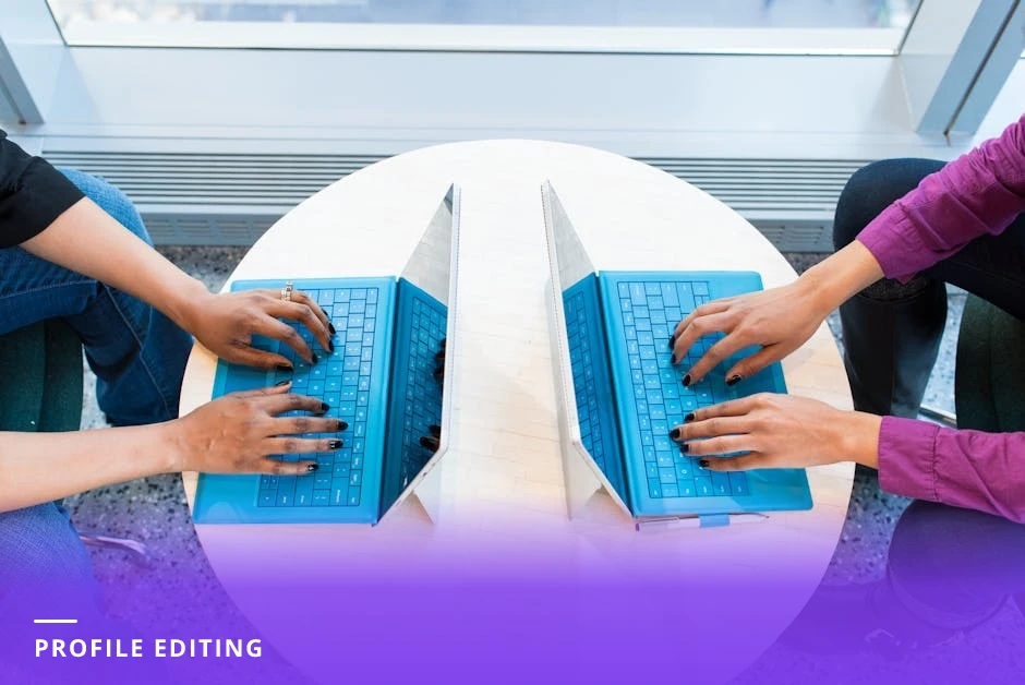 Coach seated at a modern Western-style desk typing on a laptop with a LinkedIn profile visible on the screen, natural window light, coffee cup and notepad nearby