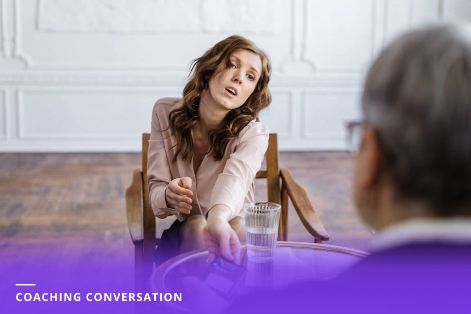 A coach and client sit at a small cafe table; the coach listens attentively while the client speaks, a notebook and pen on the table, natural window light and a candid, conversational mood.