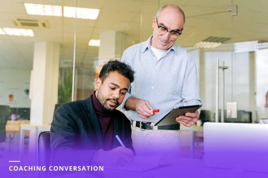 Two professionals in a modern Western office: a mentor leans forward attentively holding a notepad while the other person speaks, natural light and engaged body language conveying a coaching conversation.