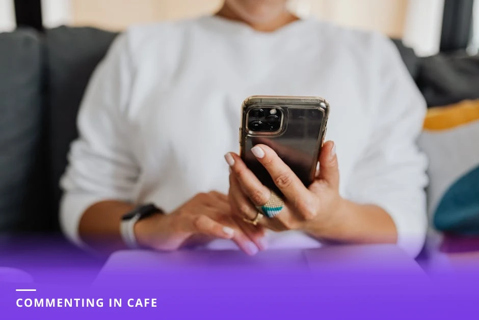 Diverse woman sitting at a bright Scandinavian-style cafe, focused and typing a thoughtful comment on her smartphone with a coffee cup on the table and natural light on her face.