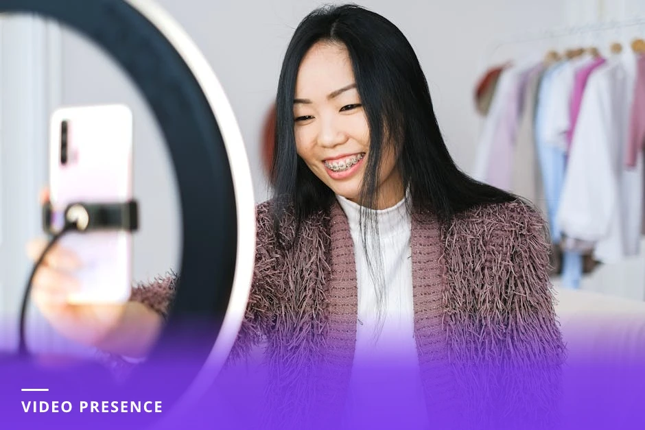 Coach holding a smartphone at arm's length, recording a casual selfie-style video in a bright modern Western office with plants and books in the background, mid-sentence expression and natural light