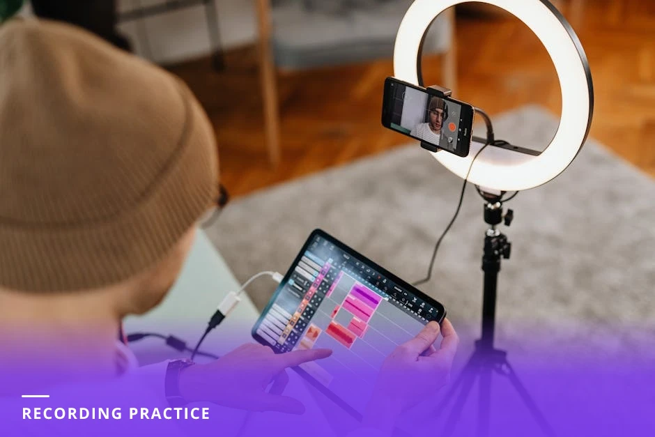Coach seated at a small home studio desk adjusting a ring light and reading notes, laptop open with a short script visible, informal warm-lit rehearsal scene
