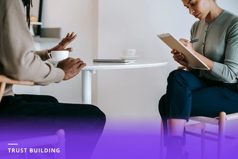 Coach and client, diverse professionals, seated at a cafe table in natural light, coach holding a notebook and pen while the client gestures, candid conversational moment