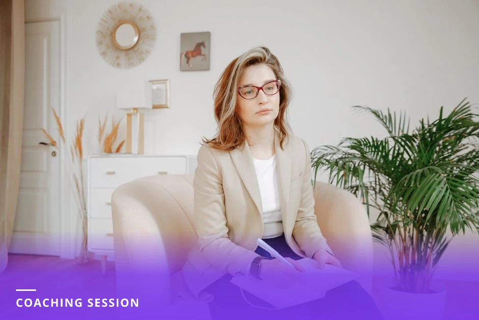 A diverse coach attentively listening and jotting notes in a notebook while a client speaks across a bright modern office table, natural window light and a laptop nearby.