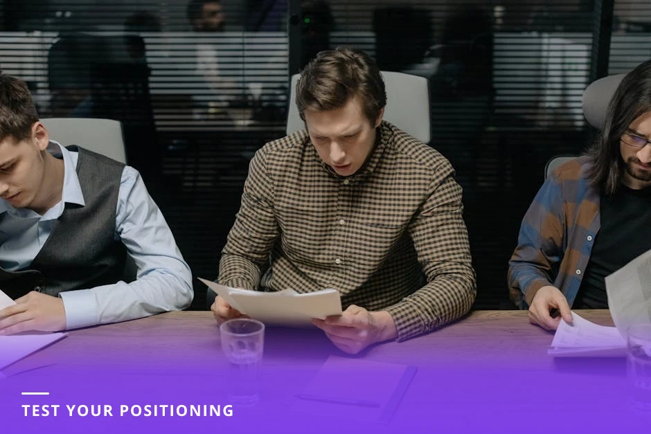 Three diverse professionals gathered around a laptop in a bright Scandinavian office, pointing at a LinkedIn headline on the screen and discussing feedback.
