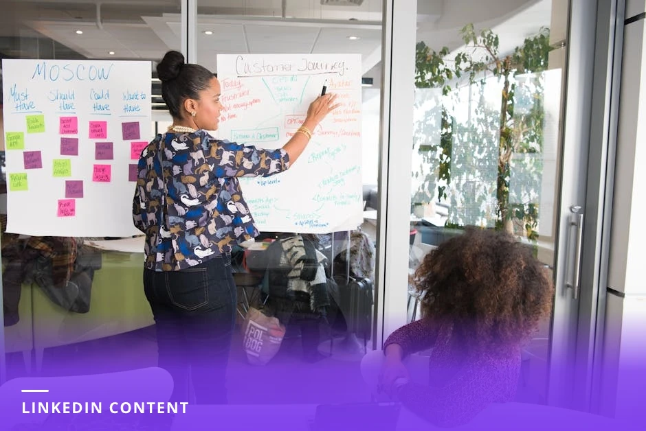 Professional at a clean modern Western desk typing a LinkedIn post on a laptop, smartphone beside showing LinkedIn feed, sticky notes and a pen nearby, warm natural window light