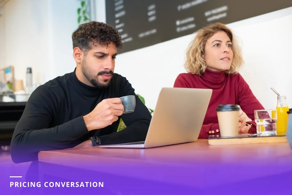 Coach and prospective client leaning over a laptop at a wooden table in a modern European cafe, reviewing notes and papers together in natural light, candid conversational moment.