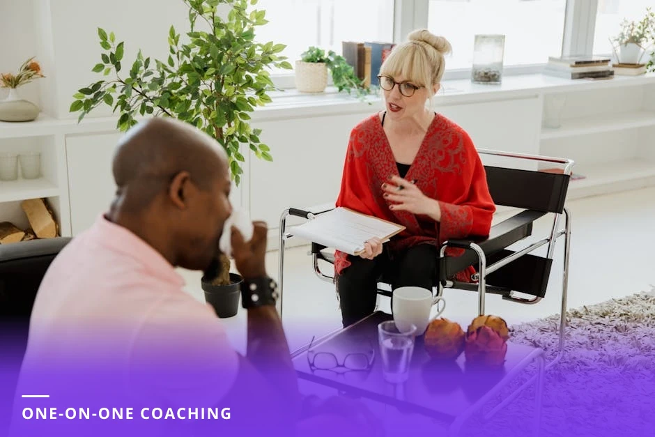 Coach leaning forward at a small urban cafe table listening to a diverse client, holding a notepad and pen while the client gestures, warm candid lighting