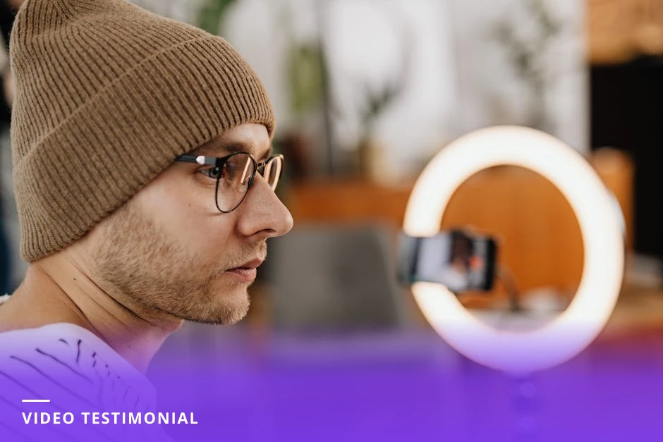 Diverse client seated in a modern office speaking to a camera with a ring light, framed and smiling as if recording a testimonial video.